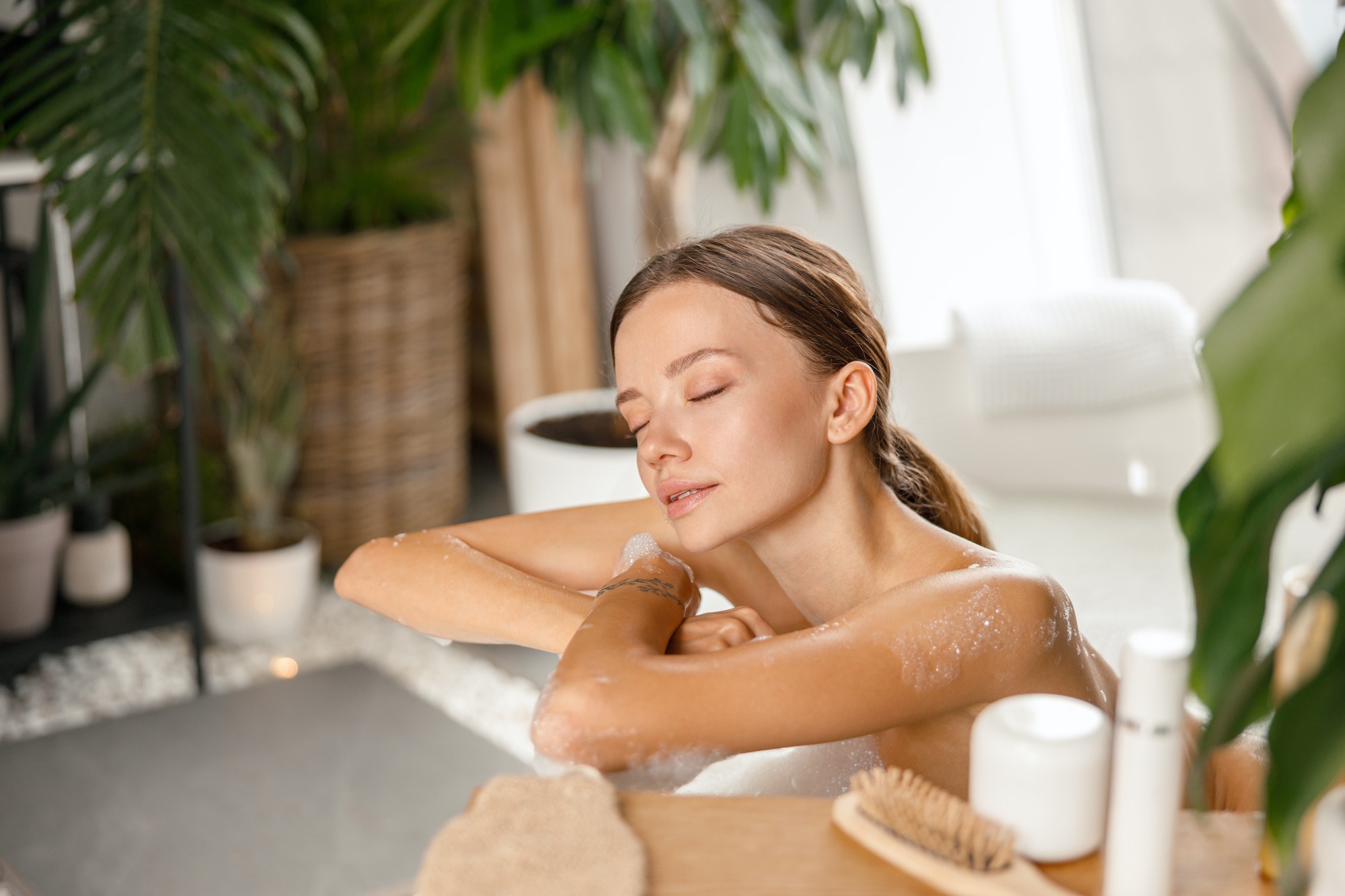 Relaxed young woman leaning on bathtub side while bathing with eyes closed at spa resort Relaxed young woman leaning on bathtub side while bathing with eyes closed at spa resort